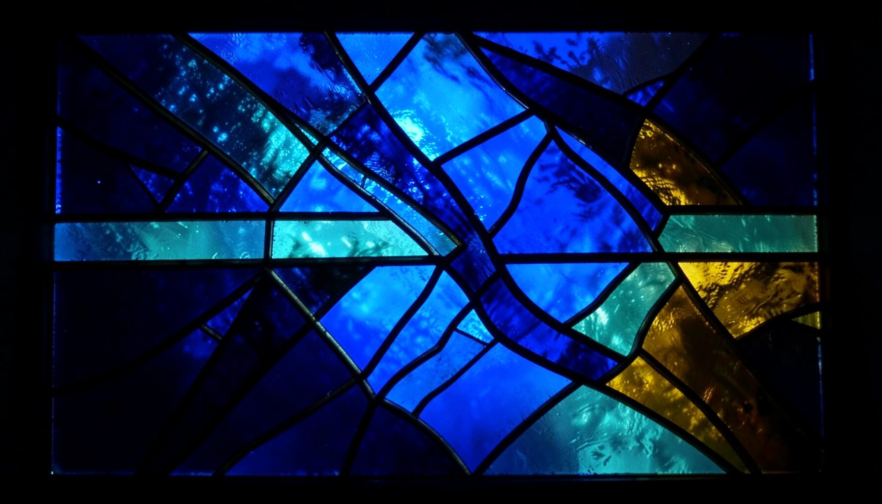 Composición en vidrieras con segmentos de plomo en tonos azul profundo, turquesa y ámbar, formando un patrón abstracto que evoca misterio y luz nocturna.